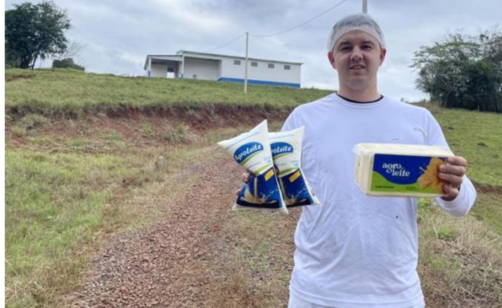 Rodrigo Angnes com leite pasteurizado e o queijo mussarela feito pela agroindústria. Ao fundo, o novo prédio, com 250 metros quadrados (Foto: Débora Kist/Folha do Mate)