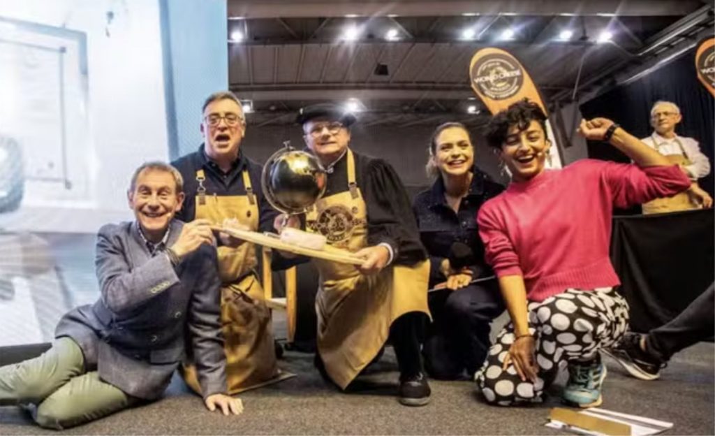 Na imagem, membros do júri e apresentadores do 'World Cheese Awards'; na tela, a espanhola Sonia Marroyo, fabricante do melhor queijo do mundo — Foto: Imagem fornecida pela organização World Cheese Awards via El País