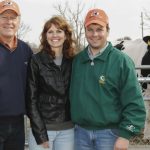 Charlie Will (à esquerda) com Brian e Wendy Fust, criadores de Fustead Emory BLITZ, na Select Sires. Atrás deles, o próprio Fustead Emory BLITZ se destaca como prova do olhar de Charlie para "diamantes brutos" — um touro que venderia mais de 1.52 milhão de unidades para a Select Sires, um recorde da empresa.